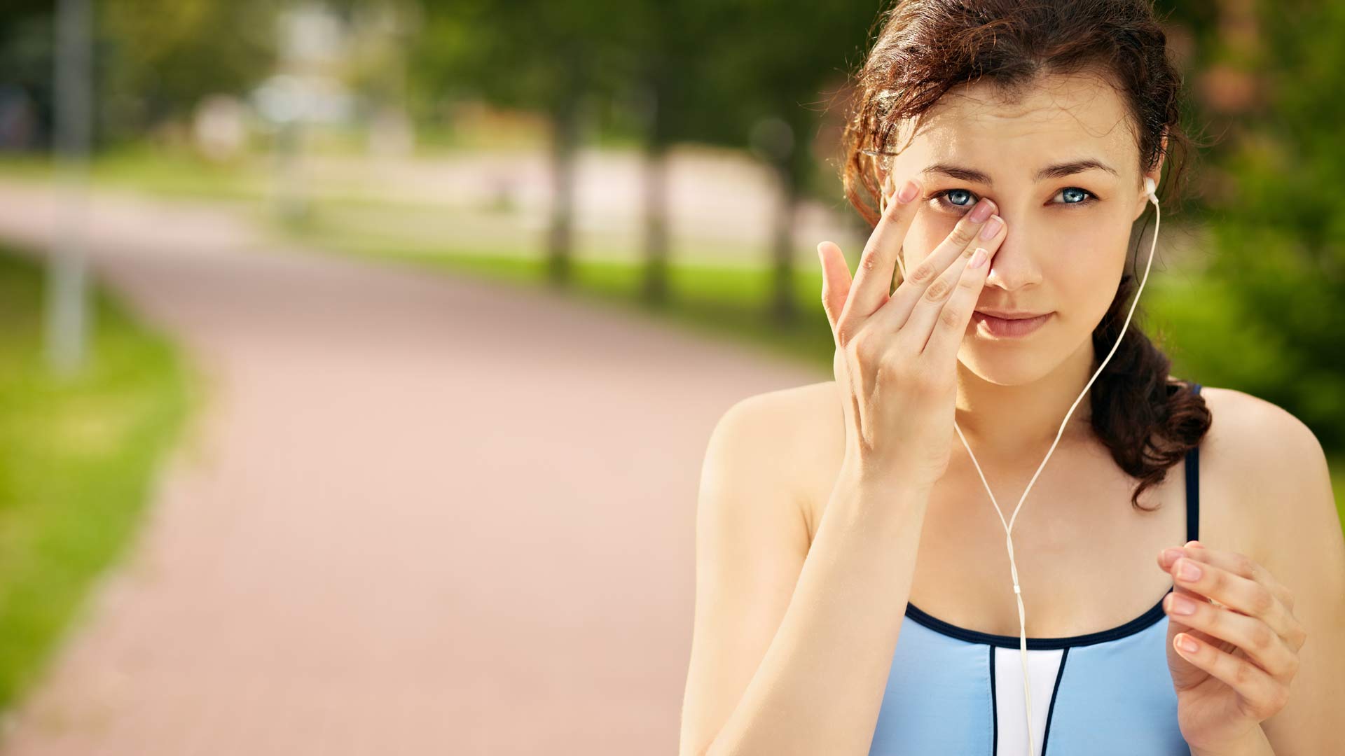 A woman touching her eye while exercising. A woman touching her eye while exercising outside on a running trail