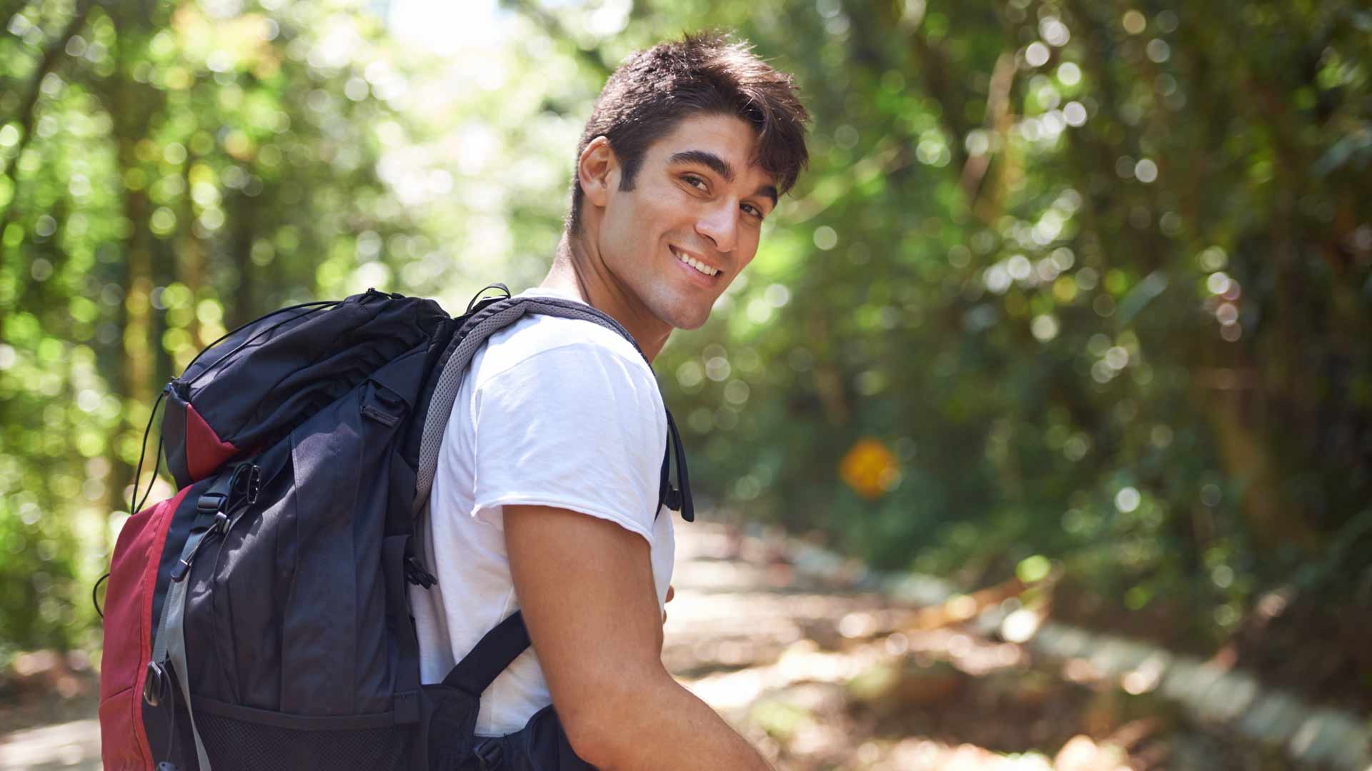 Un joven sonriente con una camisa blanca y una mochila negra en la espalda.  