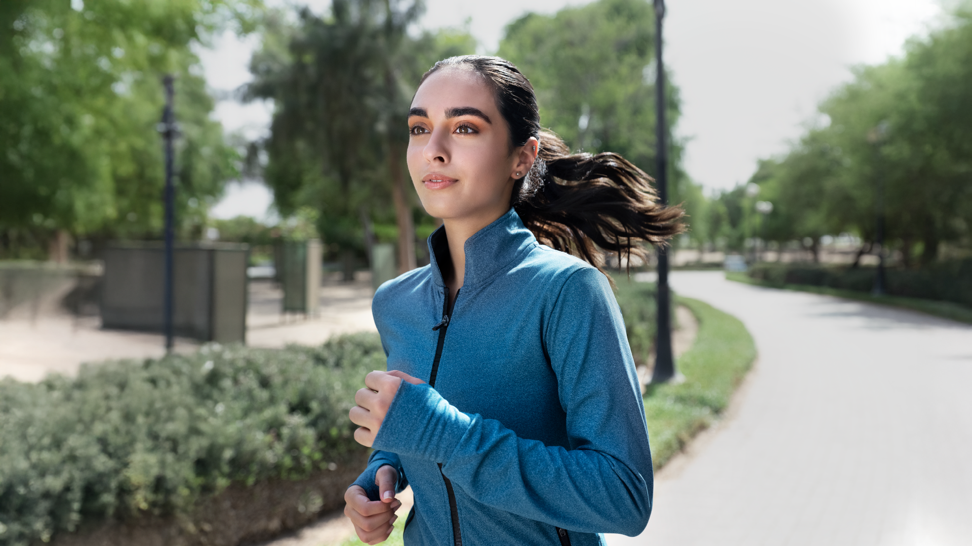 امرأة عربية سمراء ترتدي سويت شيرت أزرق تستمتع بالجري الصباحي في الحديقة