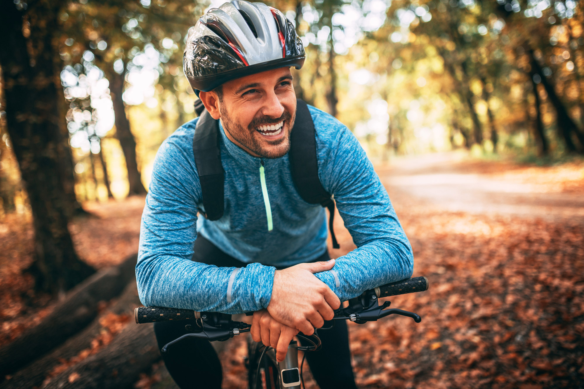 Homme souriant en bicyclette avec un casque noir et vêtu d'un chandail bleu écume de mer confortable
