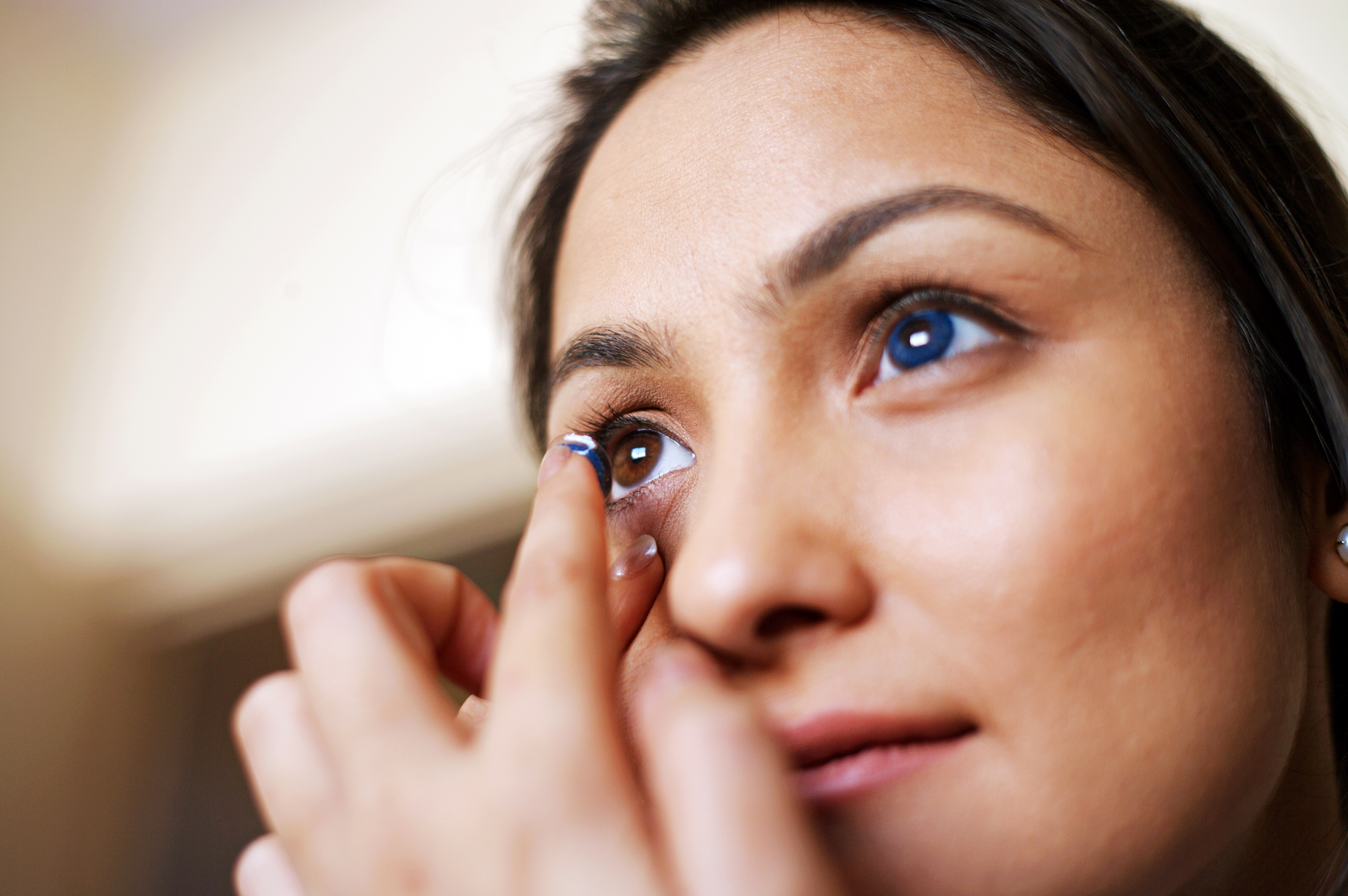 A young woman with blue eyes inserting contact lenses.