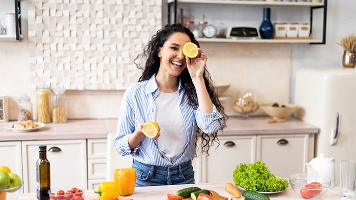 Mutfak tezgahı üzerinde sağlıklı yiyecekler görünen elinde portakal tutan mutlu kadın
