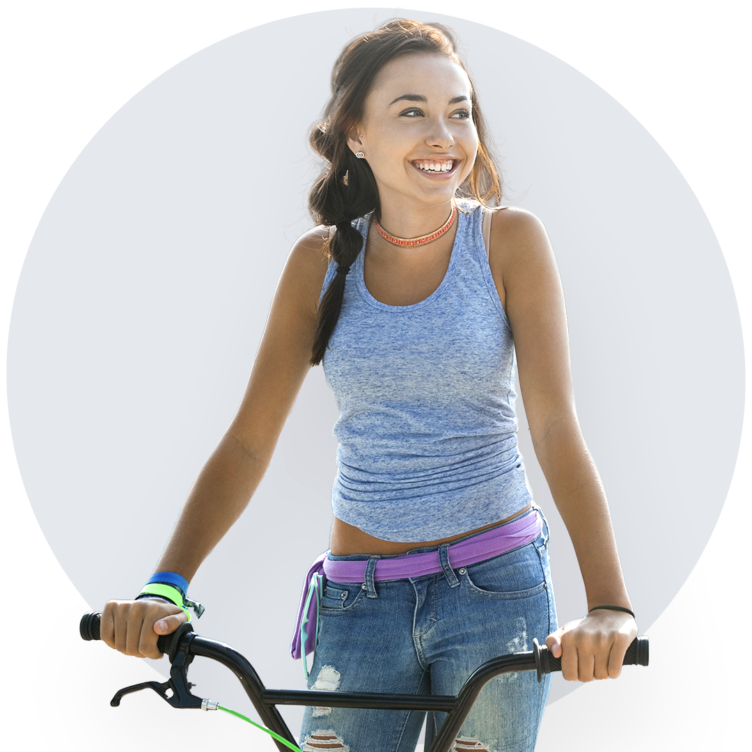 Jeune fille souriante à bicyclette, ses yeux fixant l'horizon. Vêtue d'un jean confortable et d'une camisole bleue