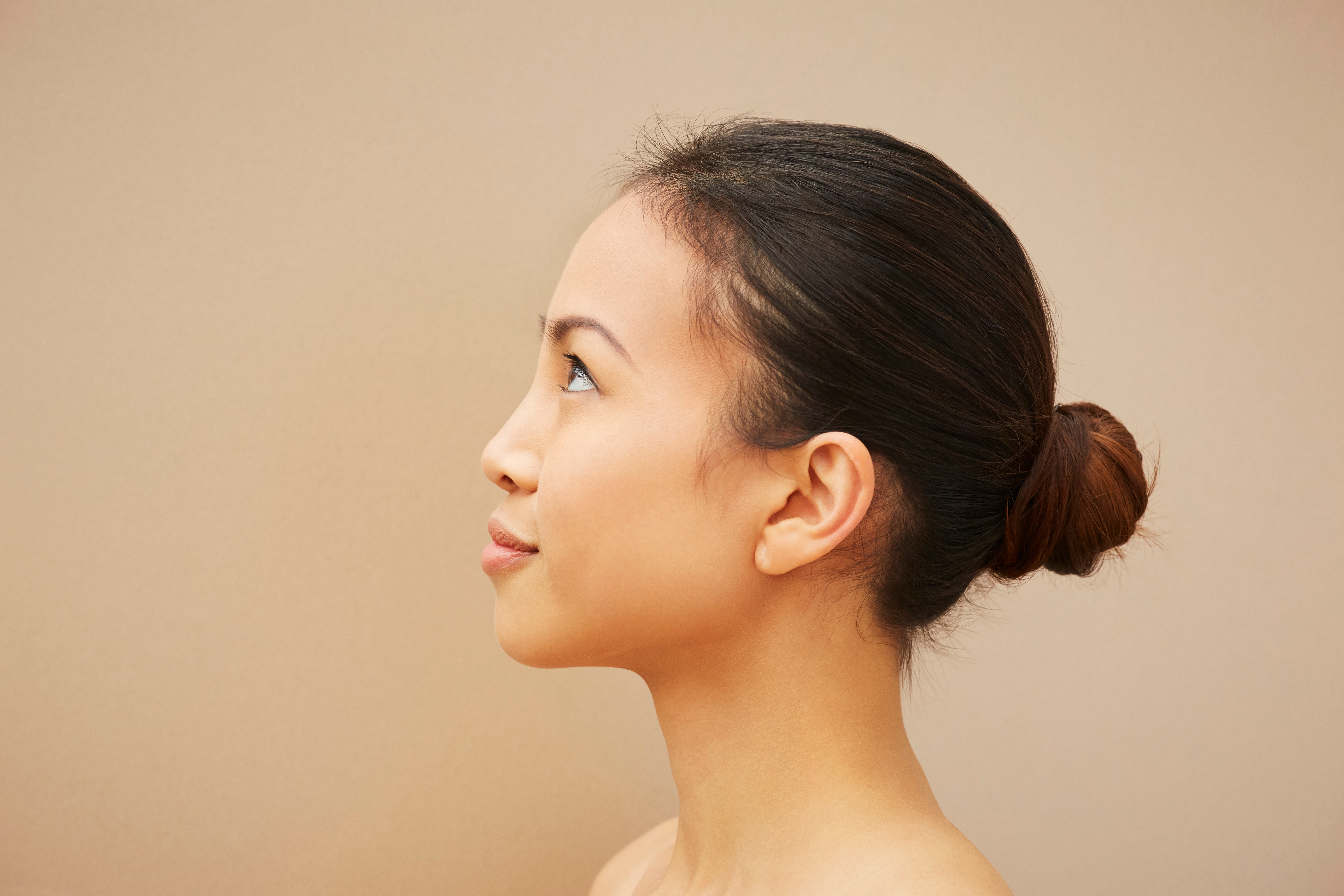 An Asian woman with bun up looking at the left side imagining