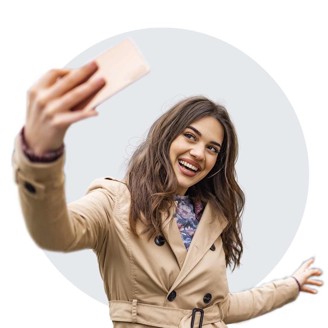 Young woman smiling and holding her cell phone while taking a selfie.