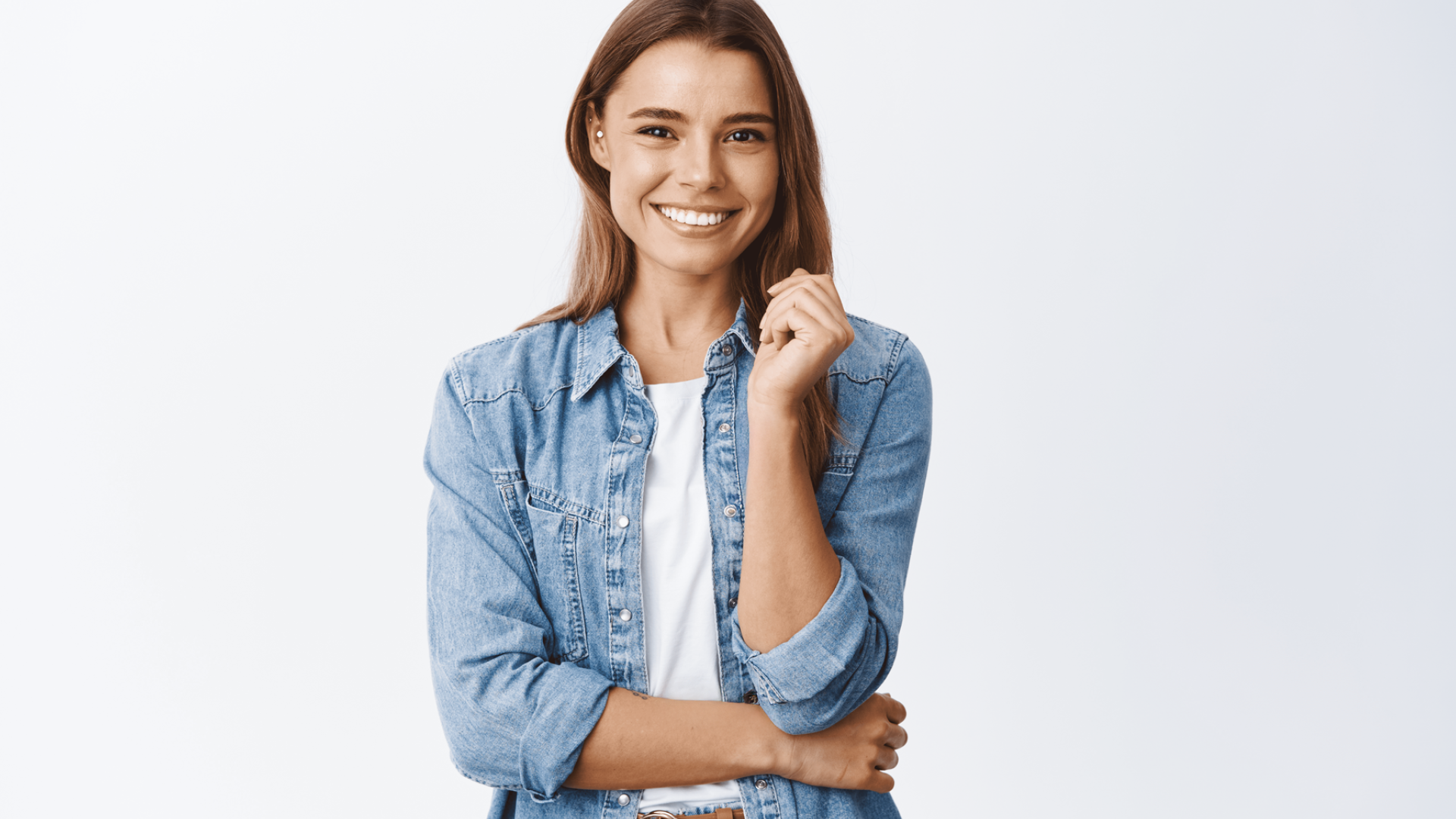 امرأة مبتسمة ترتدي قميص جينز وتيشيرت أبيض تتخذ وضعية أمام خلفية بيضاء