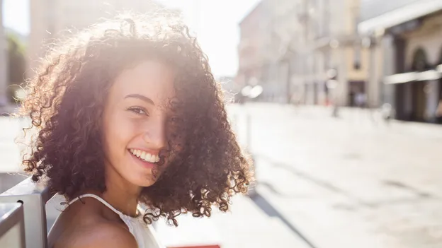 Une jeune fille aux cheveux frisés qui regarde par-dessus son épaule et qui sourit avec le soleil en arrière-plan