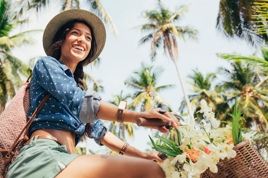 Une femme souriante dans un décor tropical avec un chapeau
