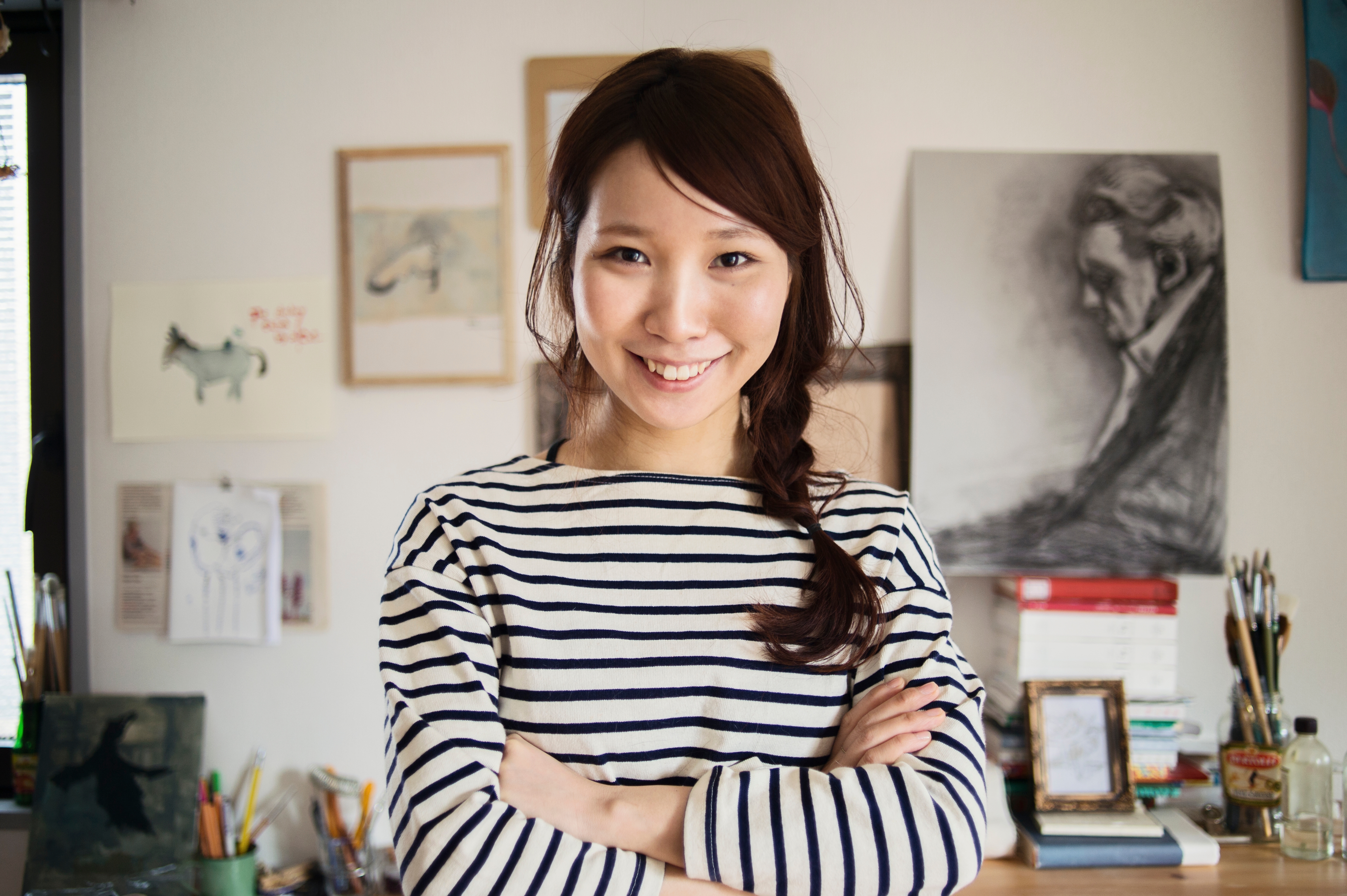 Young Asian woman with white &  black stripe blouse smiles while looking at the camera.