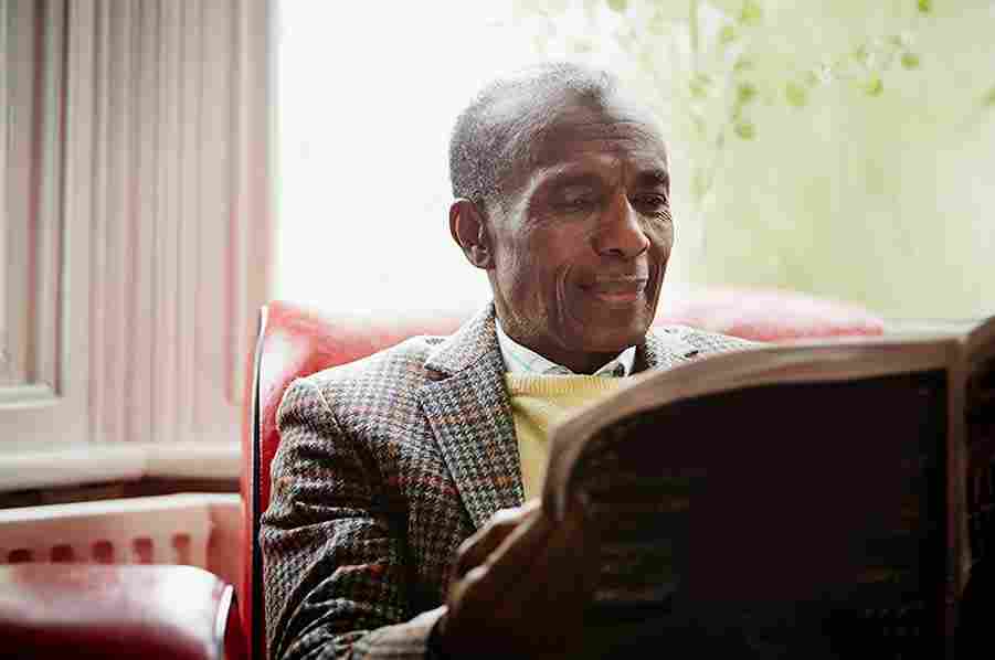 A smiling black older gentleman reading a newspaper  