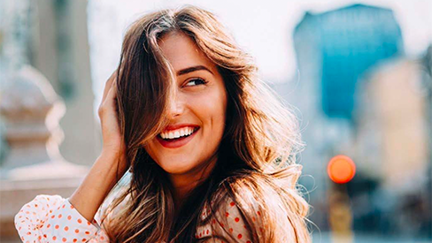 Donna felice e sorridente che indossa una camicia a pois e con capelli castani che coprono un occhio