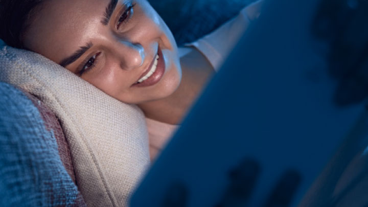 Eine lächelnde Frau schaut auf ihr Tablet in dunkeln an Eine Frau schaut auf ihr Tablet in dunkeln an