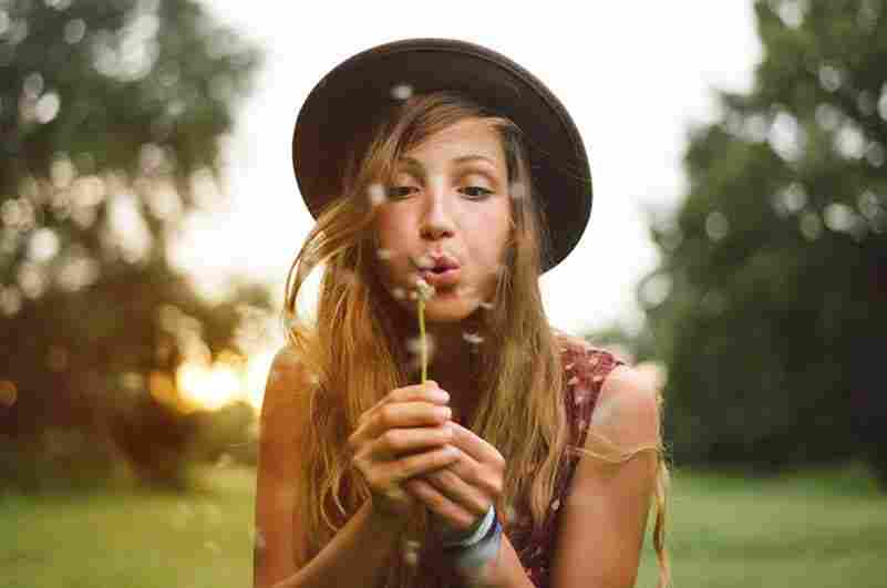 Woman with hat blowing on a dandelion  