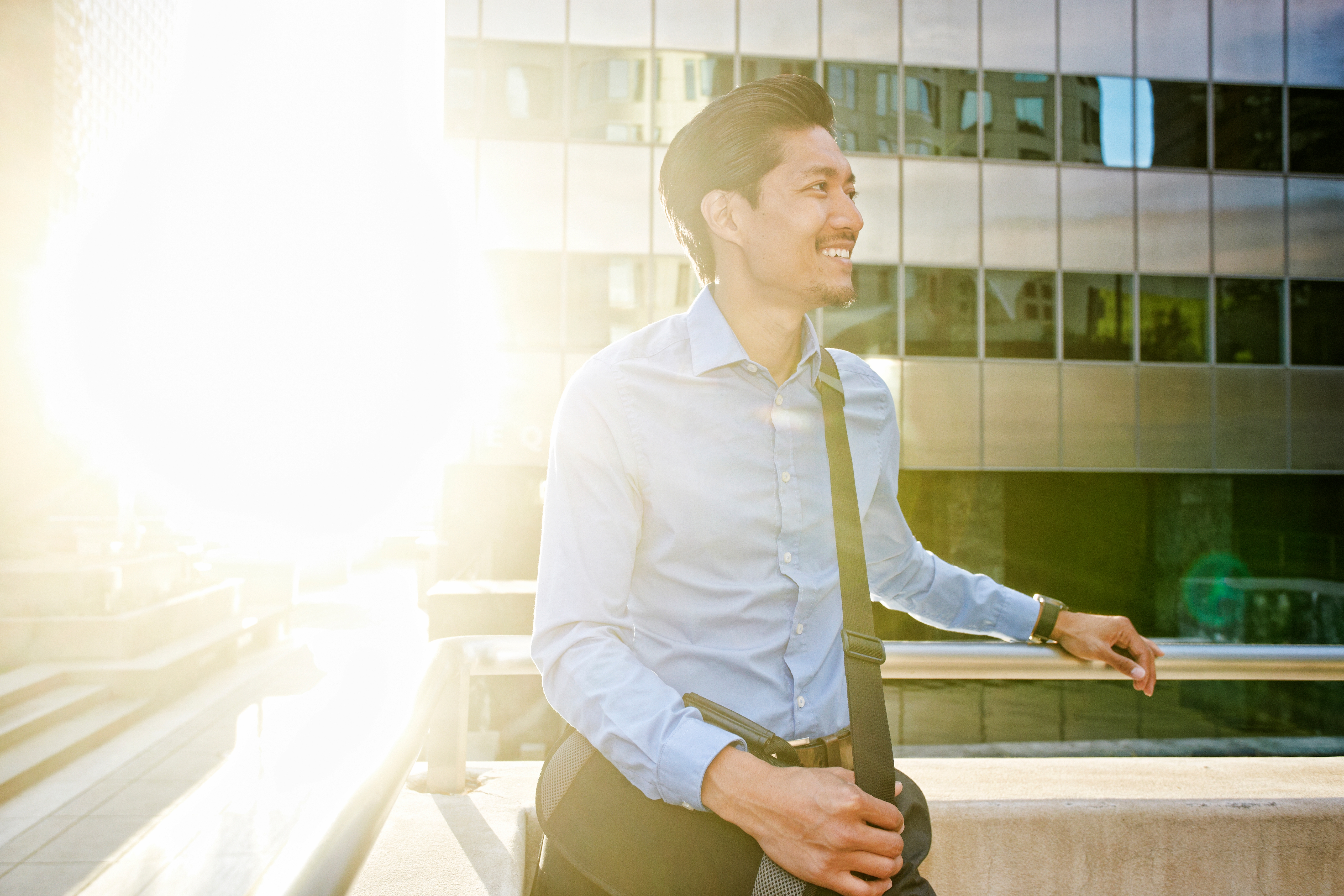 A young working man with working attire looking at the side and smiling at the top of a building.