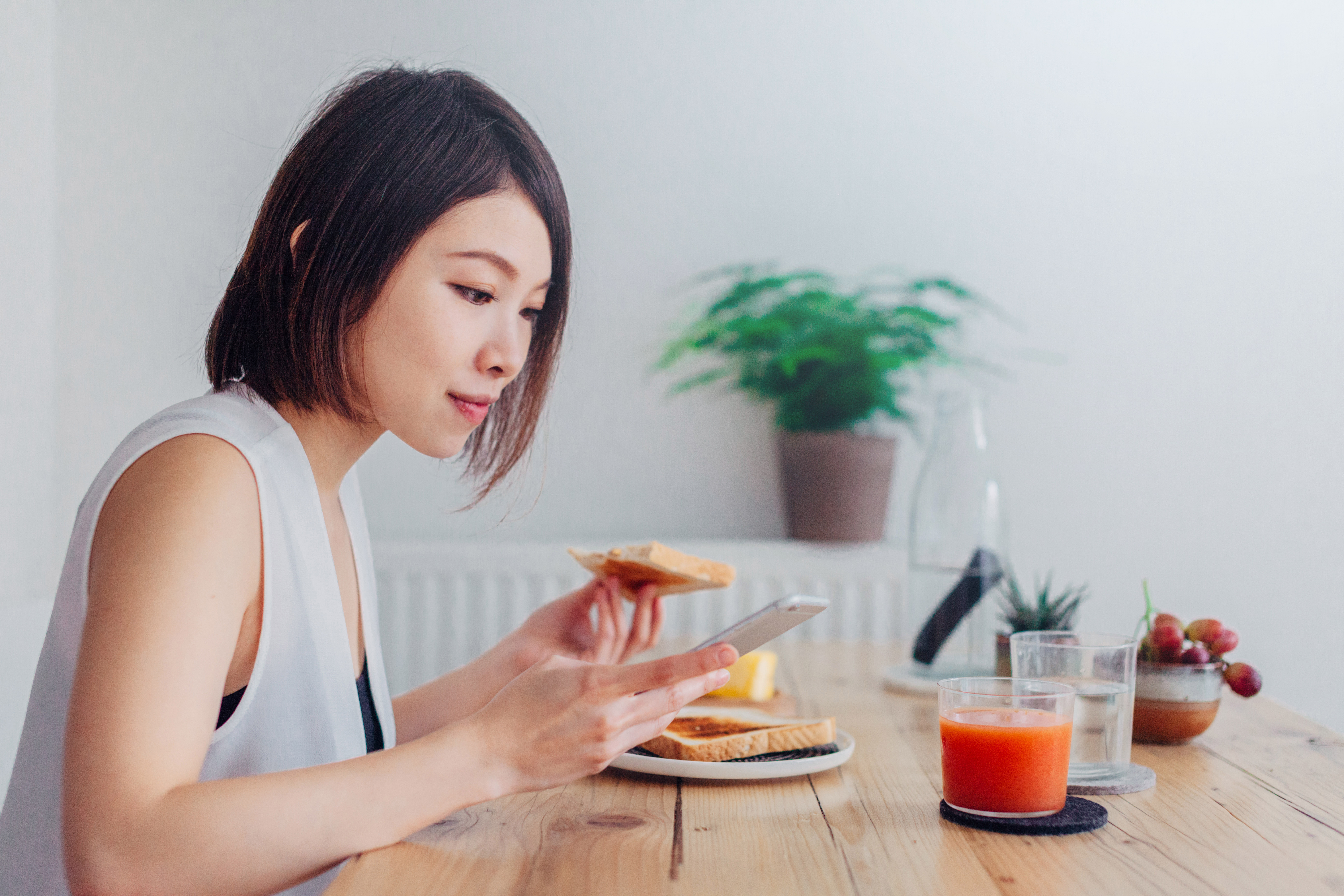 Asian woman eating toast while looking at her phone.