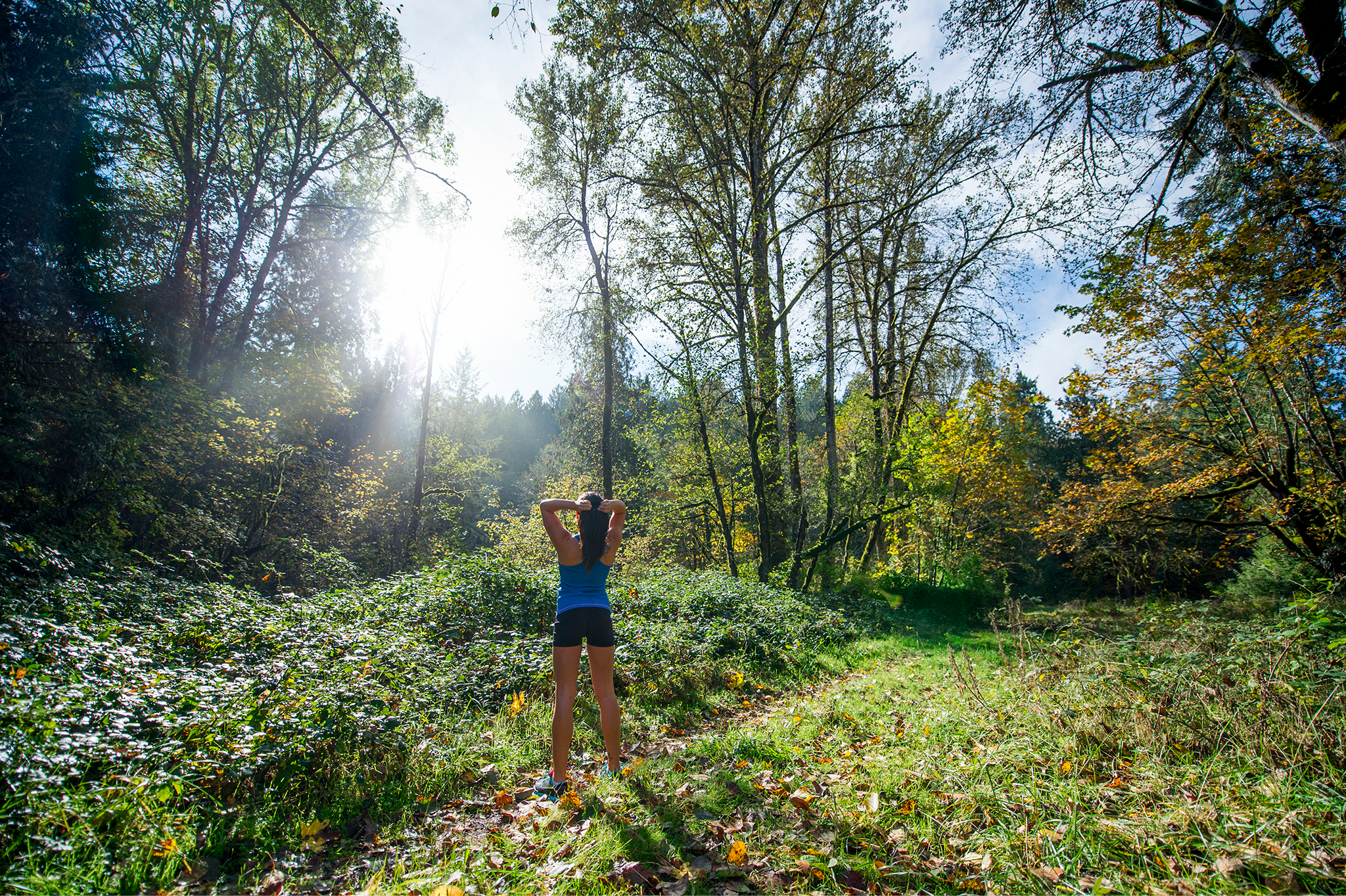 A woman hiking in the forest with sunlight beaming through the trees.