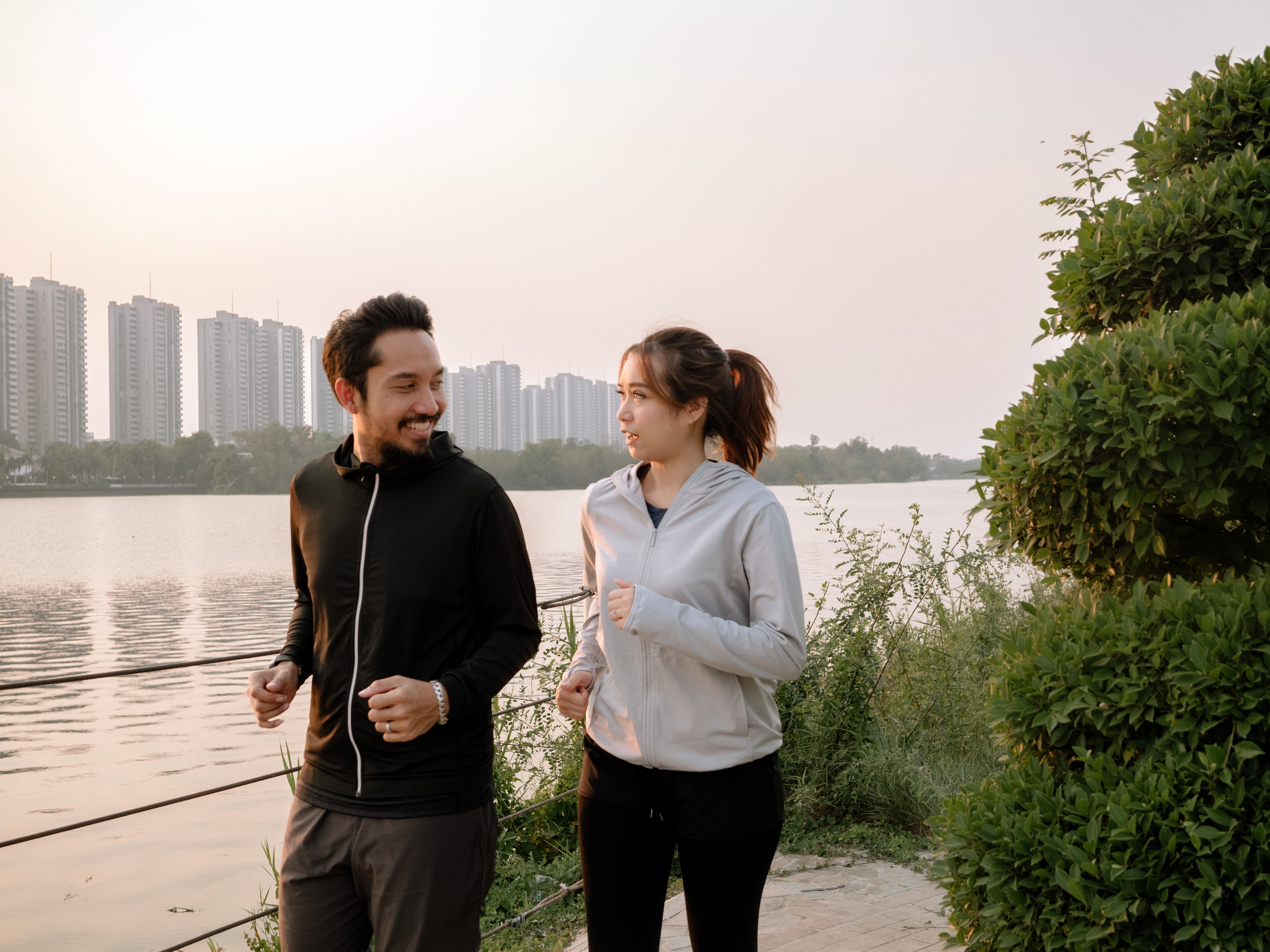 Two individuals jogging along the river while the sun is going down