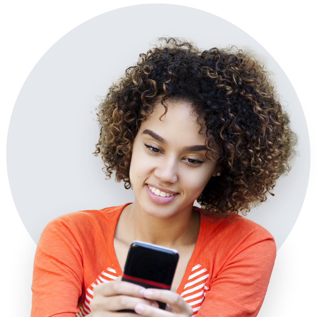 Smiling young woman with natural hair wearing an orange striped shirt, looking at the cellphone in her hands.