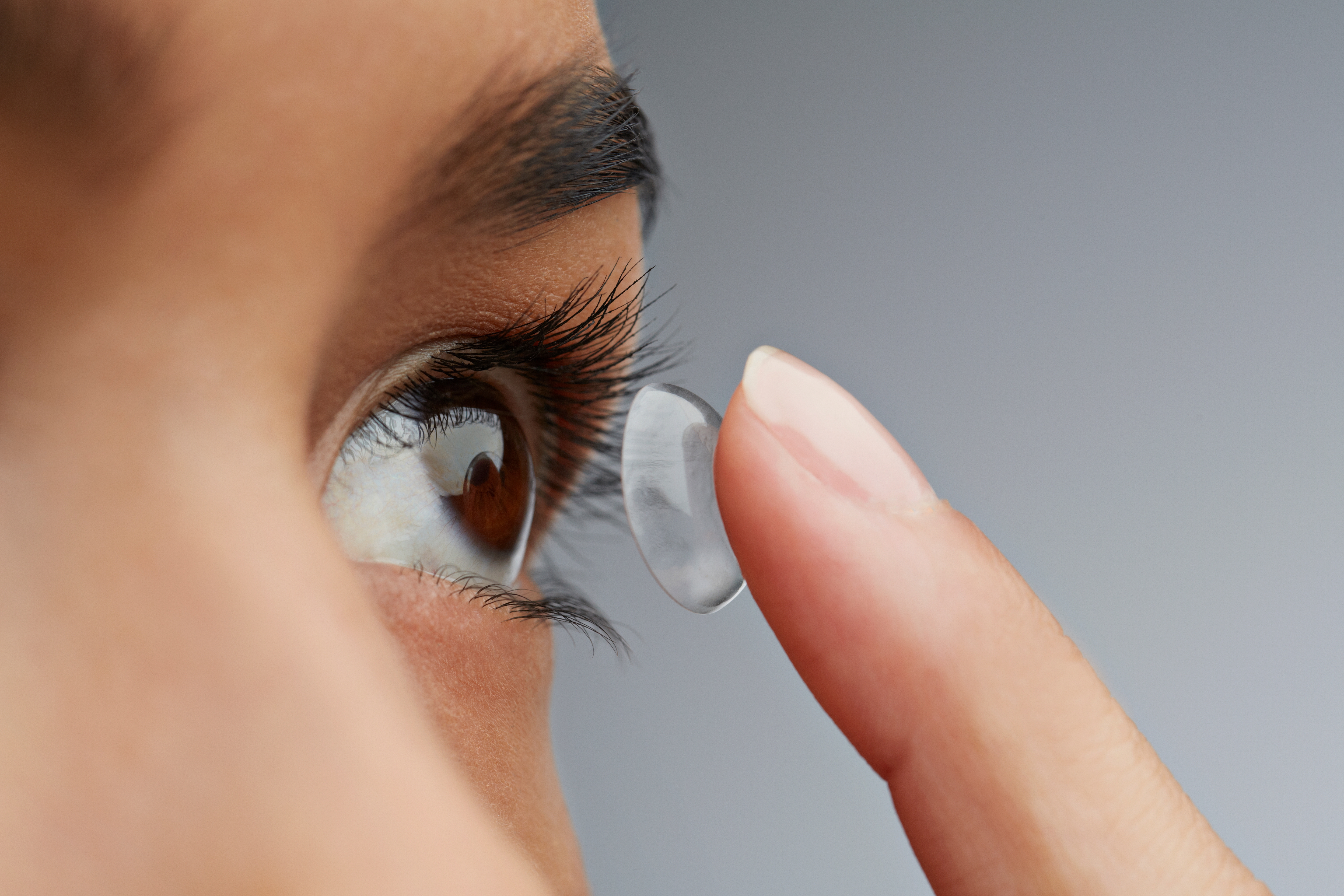 A young woman putting on Contact lenses while looking at the mirror.