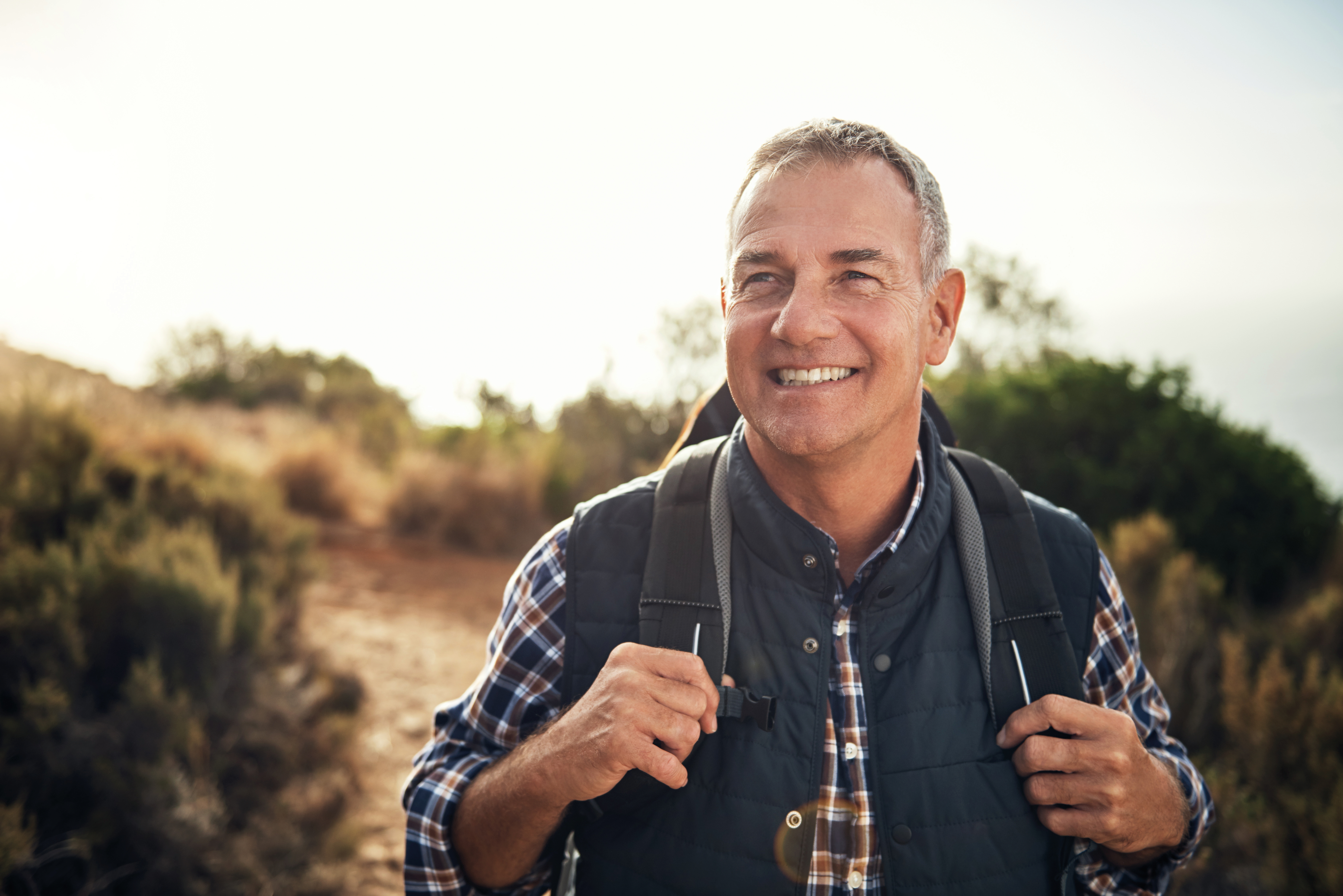 Hombre con un pelo gris con una mochila sonriendo mientras hace una caminata