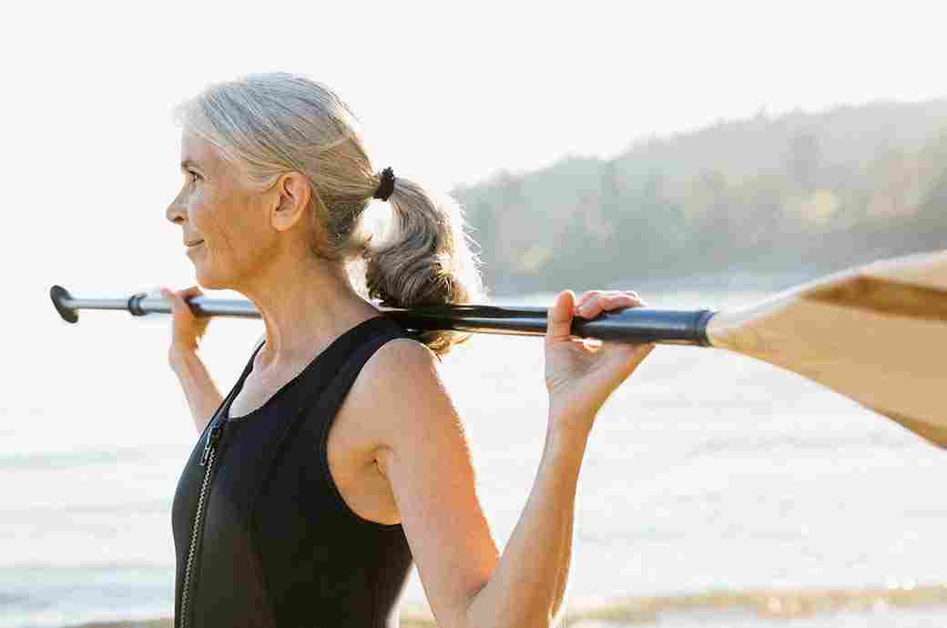 Femme âgée à l’extérieur sur la plage avec une pagaie