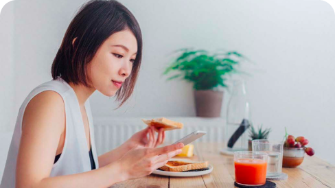 Donna asiatica che fa colazione a un tavolo mentre guarda il suo telefono