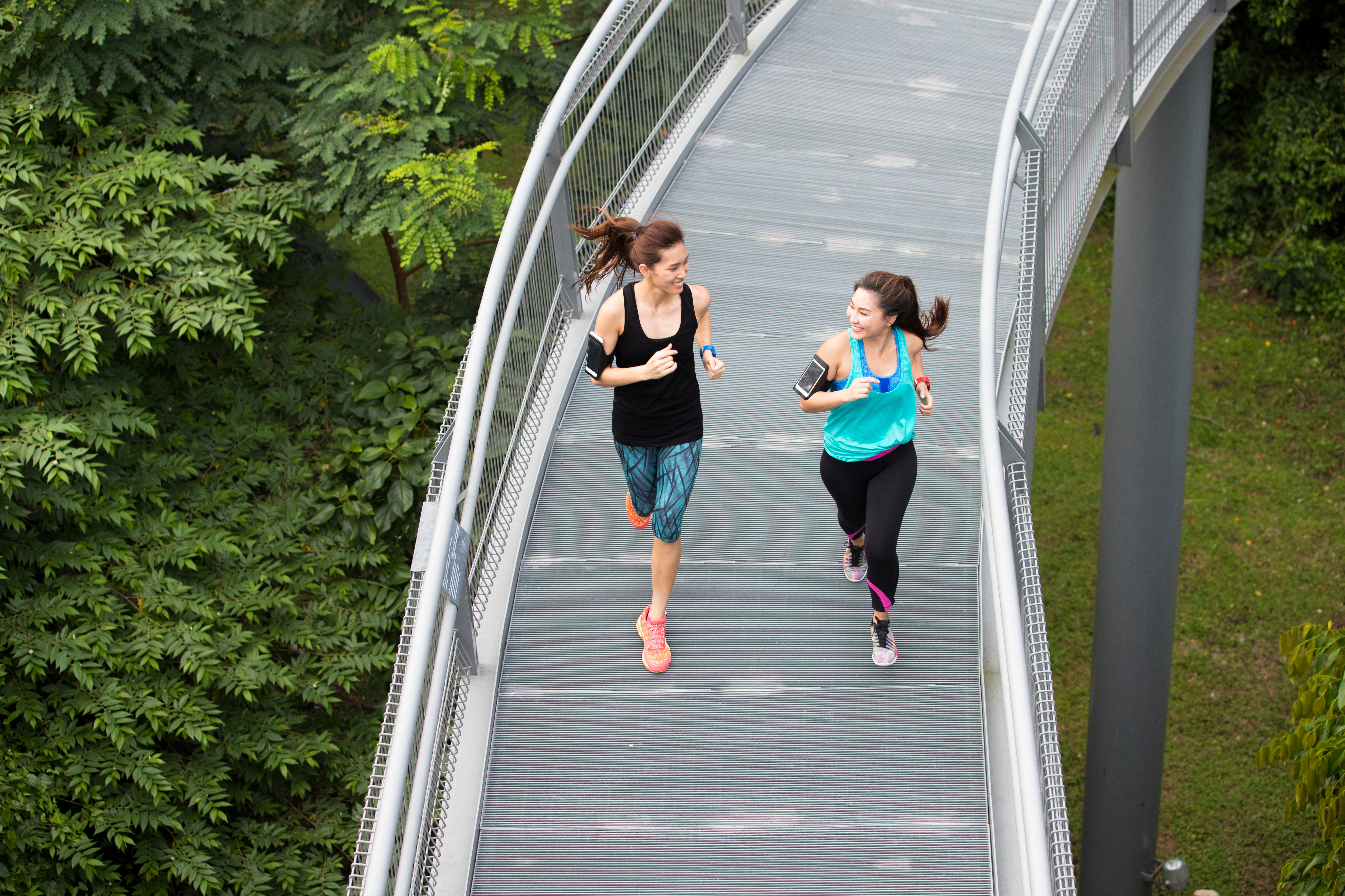 Two young women running and smiling at each other on the bridge at the park