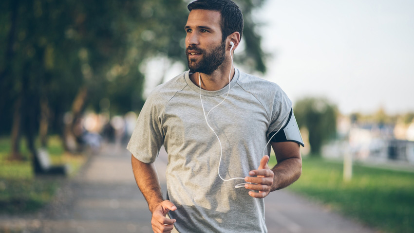 Homem jovem praticando esportes vestindo uma camiseta cinza, olhando para a direita no meio da rua. 