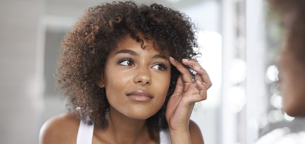Black woman with brown eyes and natural hair inserting contact lens.