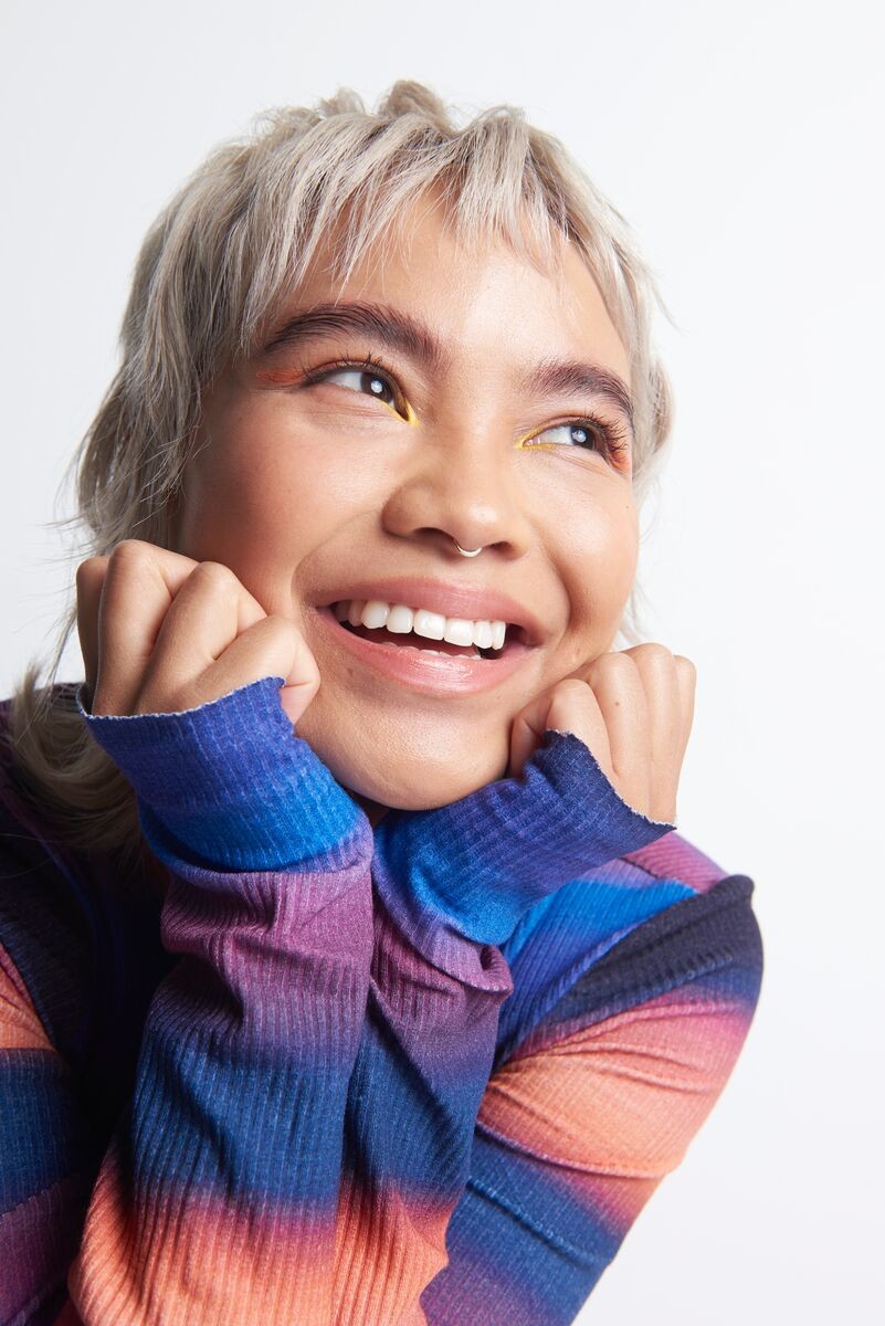 A picture of a young blonde haired woman with her hands on her face smiling and looking away from camera