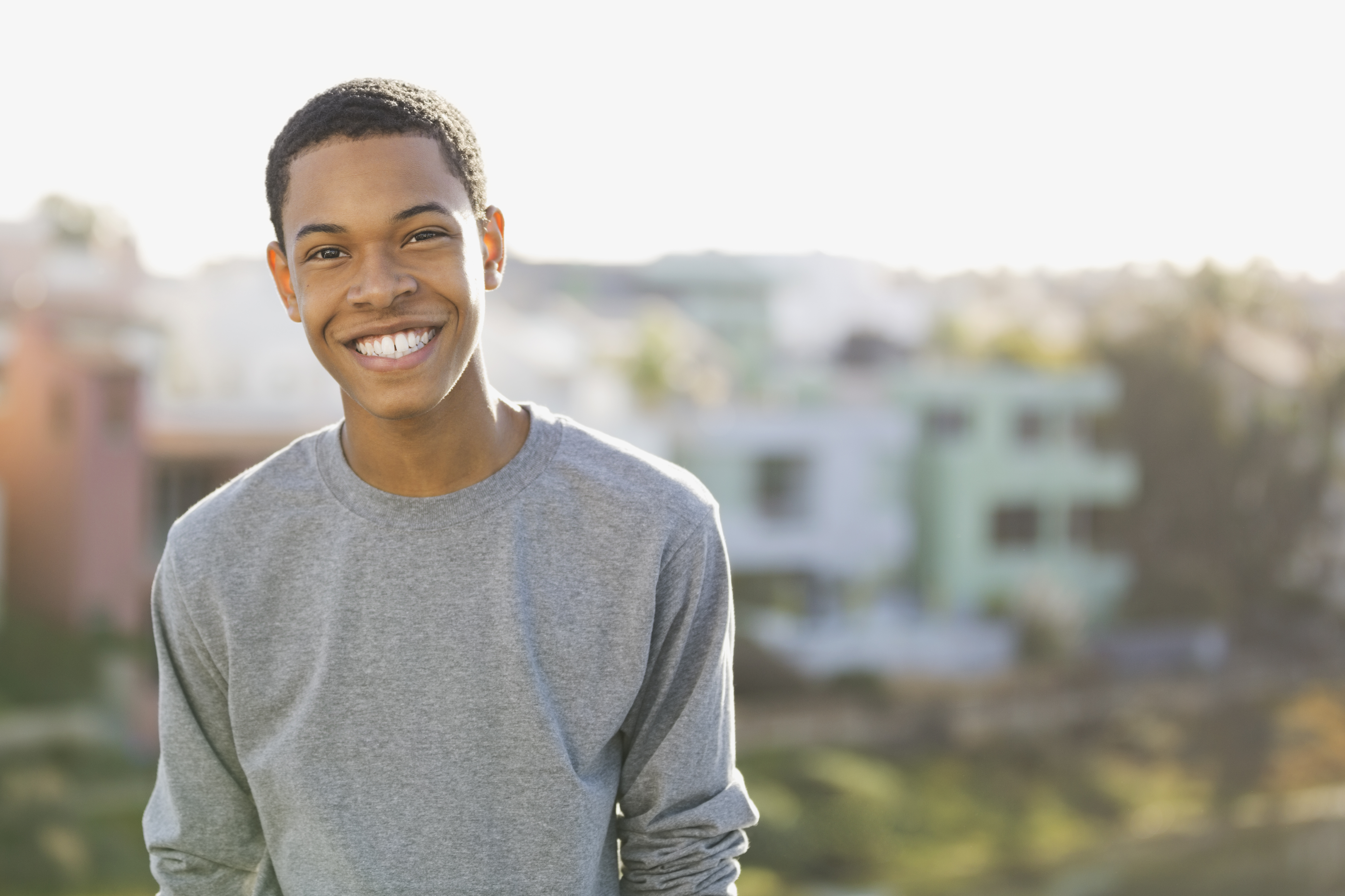 Black teenager in a gray t-shirt smiling and looking directly at the camera.