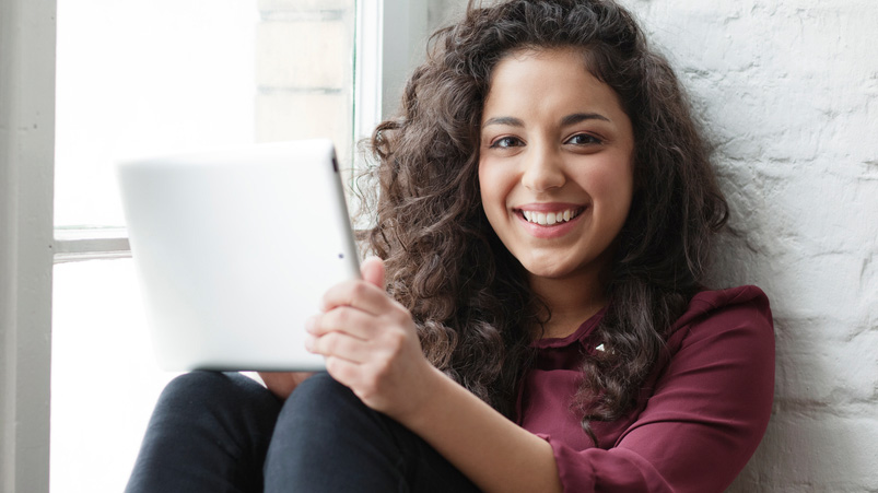 Joyful woman with wavy hair in maroon blouse, holding a tablet.