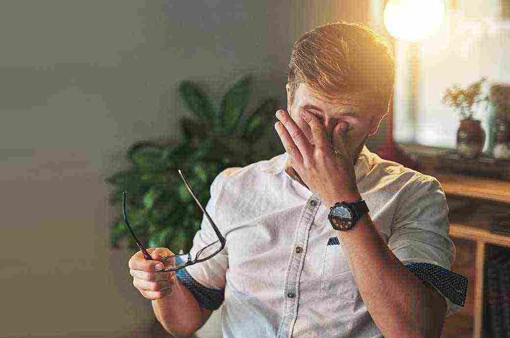 Homem sentado em uma cadeira coçando os olhos 