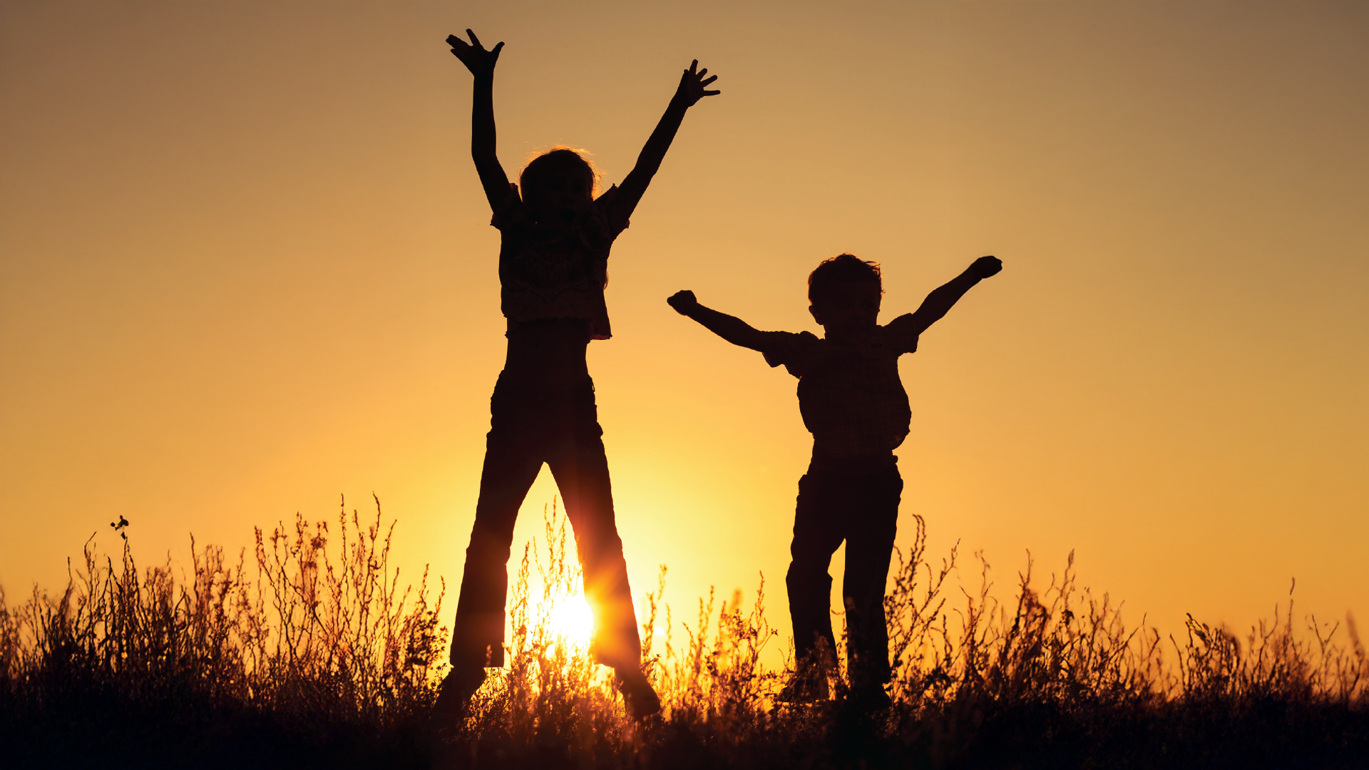 أطفال أو مراهقون يقفزون في الهواء عند غروب الشمس، أيديهم تتطاير، يصنعون فن الظلال ضد السماء النابضة بالحياة