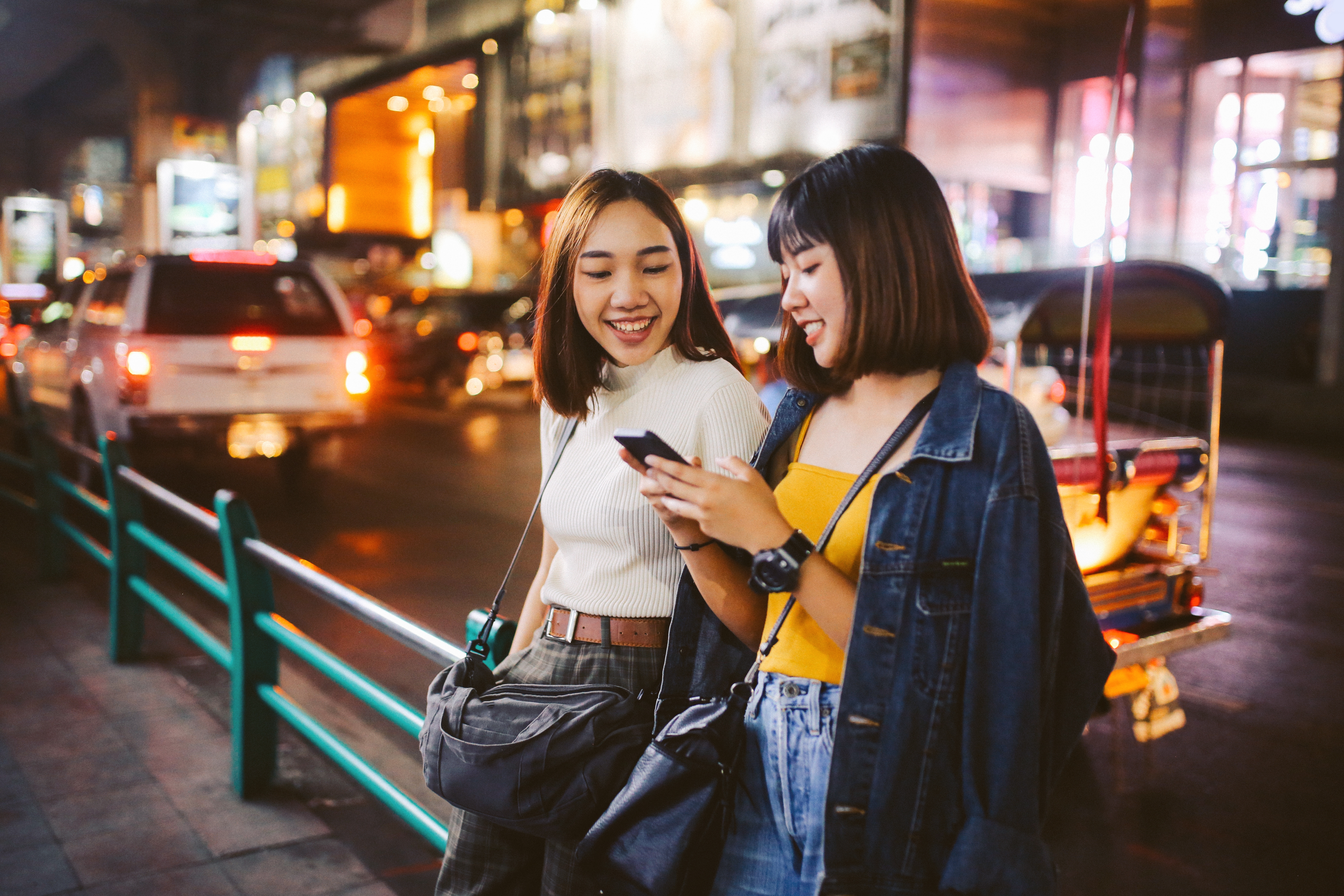 Two Young teens looking at the cellphone with a smile on the street at night