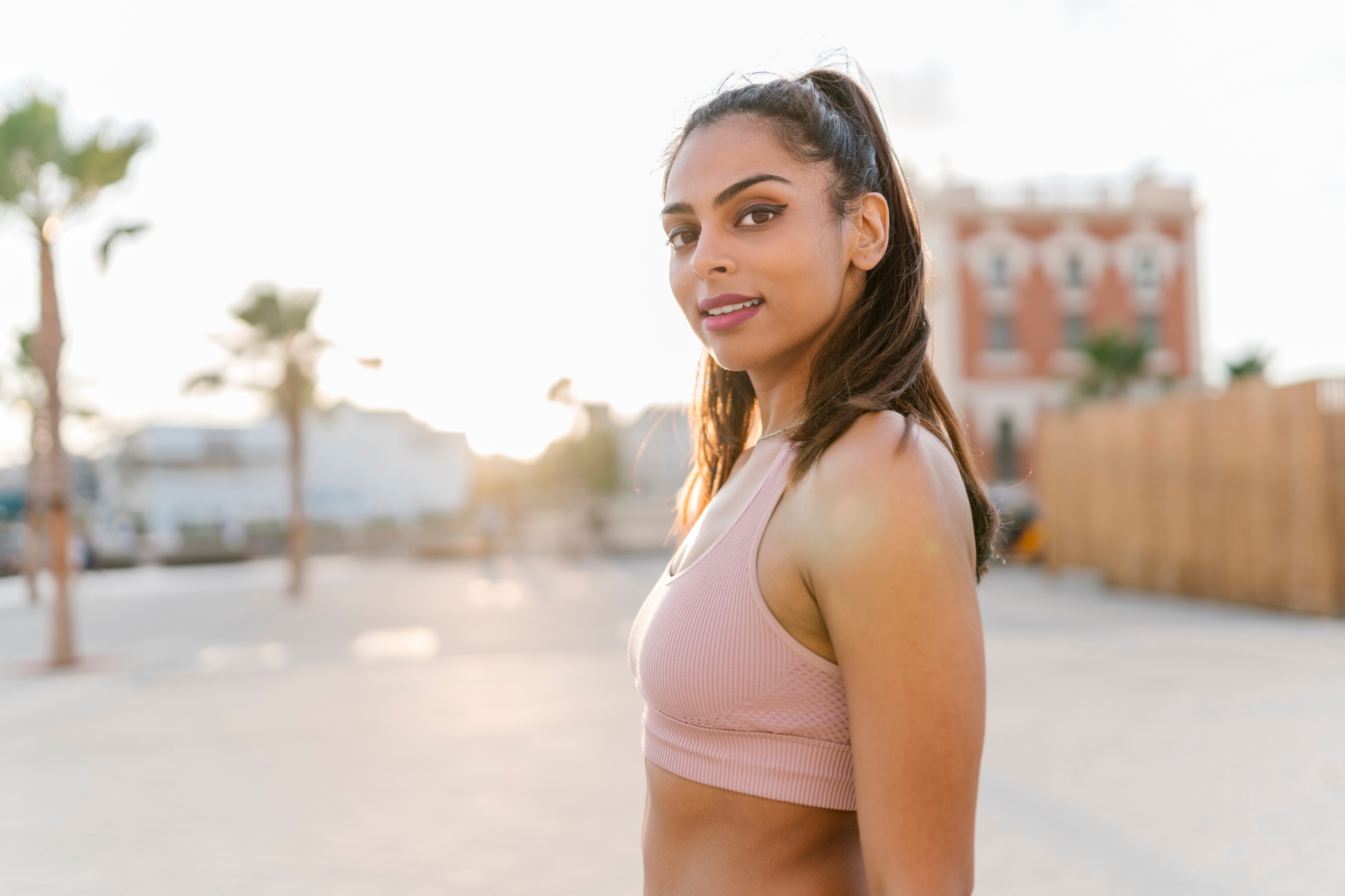 A young with ponytail girl smiling looking over her shoulder and smiling with the sun in the background