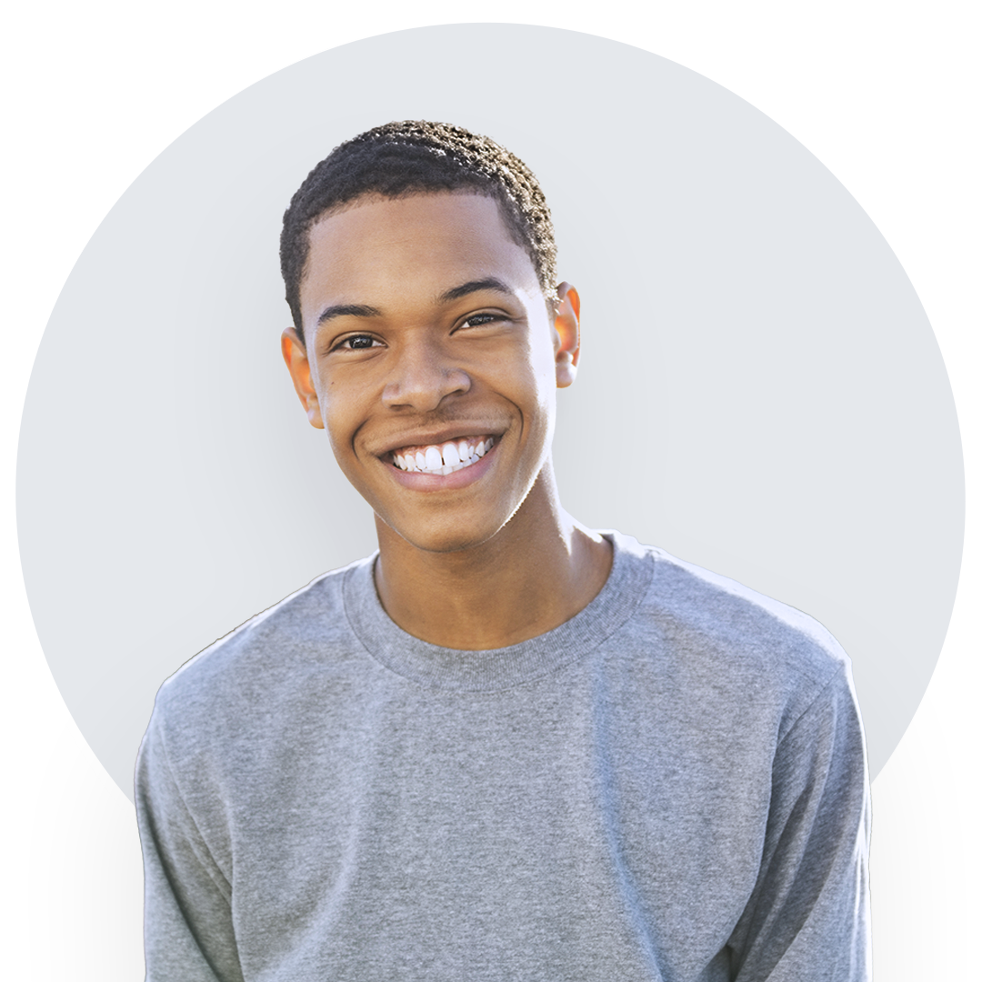 Black teenager in a gray t-shirt smiling and looking directly at the camera.