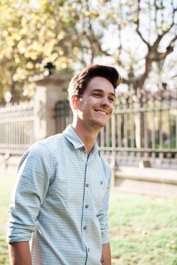 Un jeune garçon souriant regarde attentivement à l'horizon et est vêtu d’une chemise bleu pâle