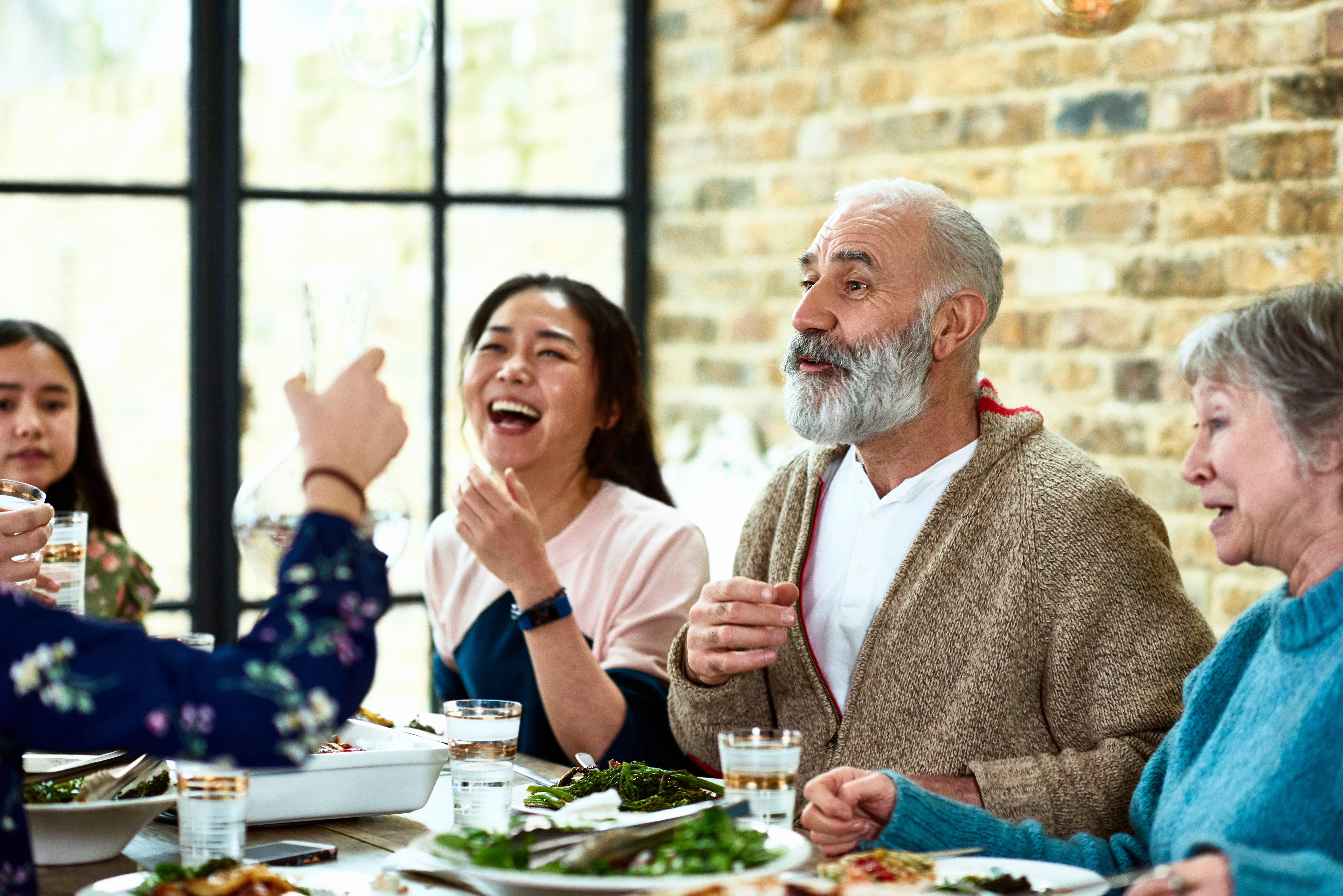 A family with 2 young teens and an old man smiling together while enjoying the food.