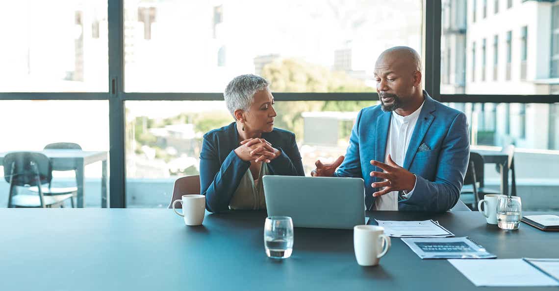 male and female sales professional sitting at a table looking at a laptop discussing their opportunity pursuit strategy