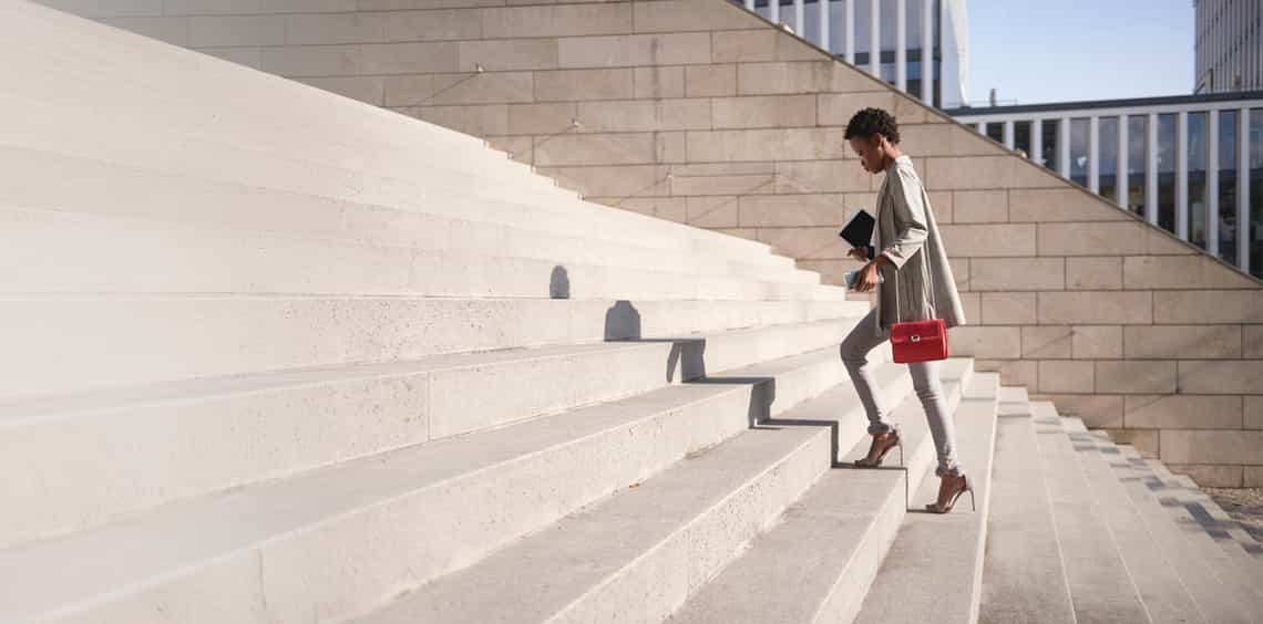 confident sales woman walking up the stairs on her way to a meeting with clients where she is going to use the Challenger approach to drive the deal forward