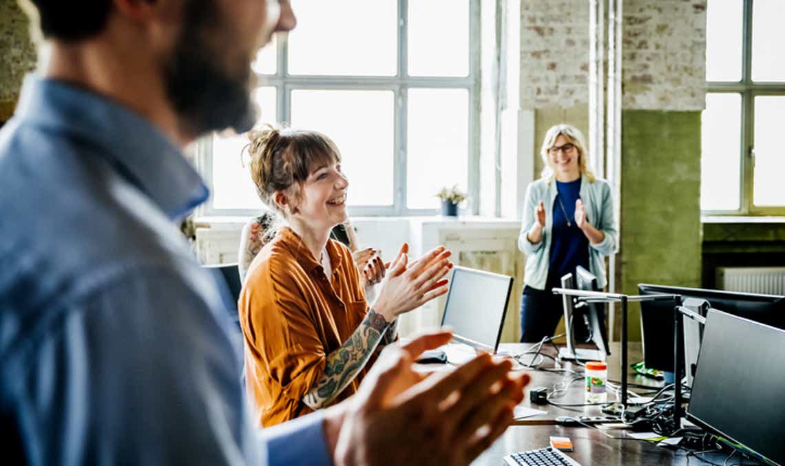 A team of sellers in an open-concept office space celebrating another team win from their desks. The win is a result of a strong sales culture.