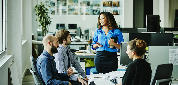 Businesswoman leading informal meeting with colleagues at office workstation using sales growth strategies.