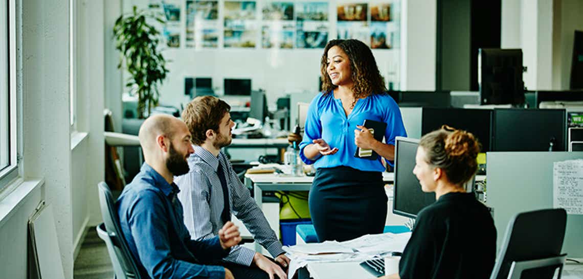Businesswoman leading informal meeting with colleagues at office workstation using sales growth strategies.