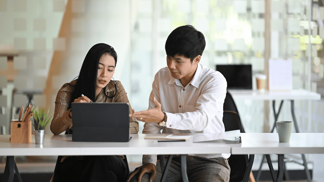 A sales manager coaching a seller at a laptop during a training session