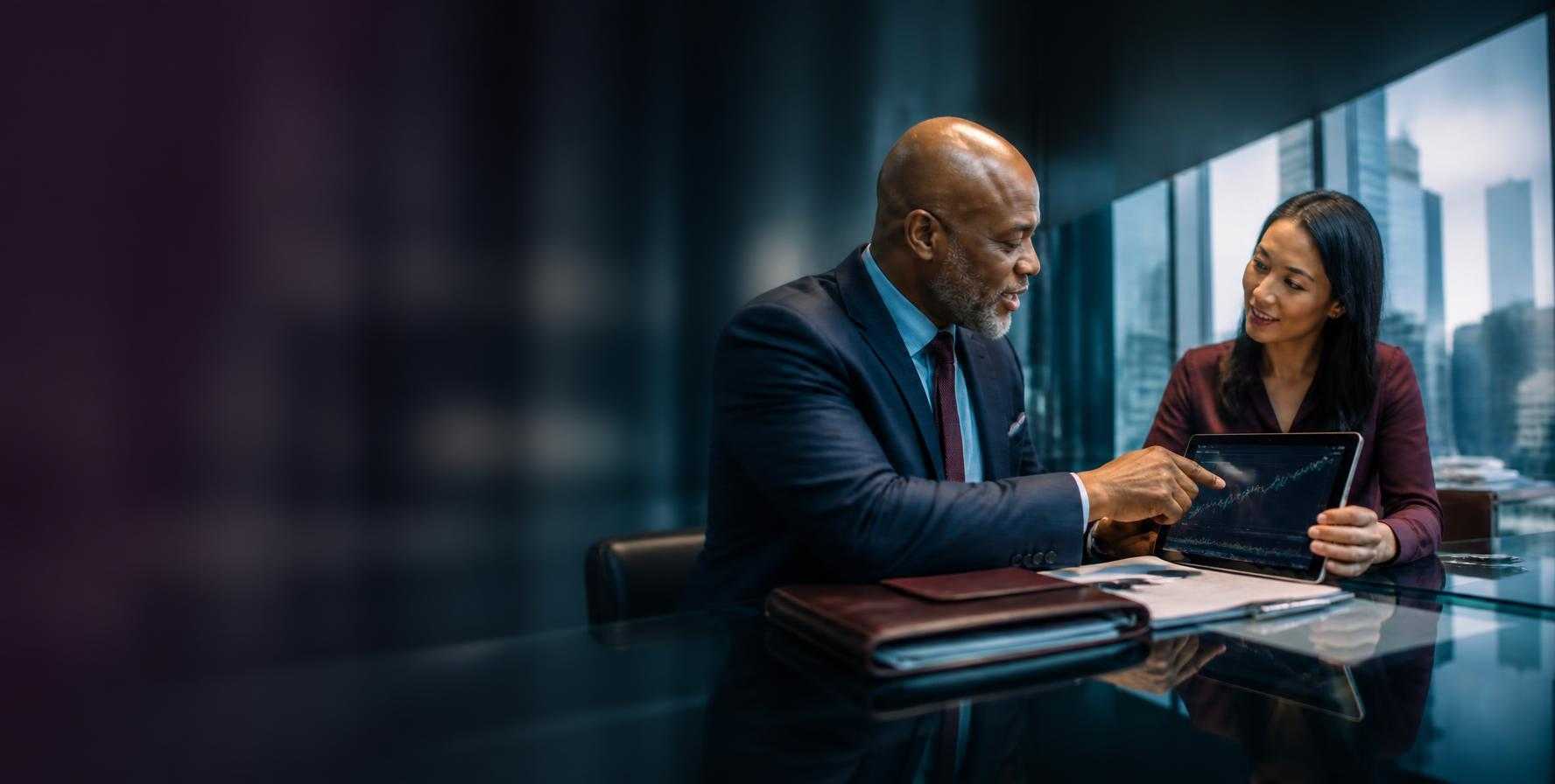 A financial advisor points to a market chart on a tablet while a client listens, in an office overlooking city towers