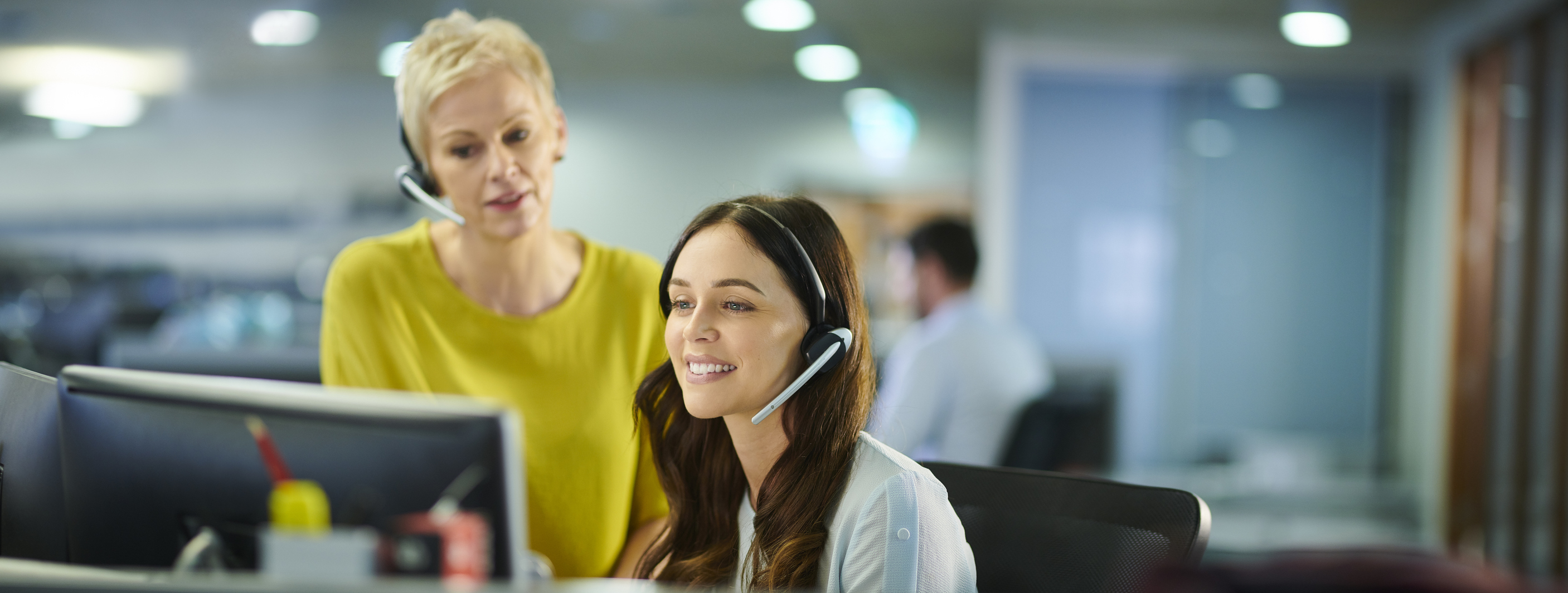 customer success associate and her manager at a computer with headsets on - practicing capabilities developed following a customer success competency framework