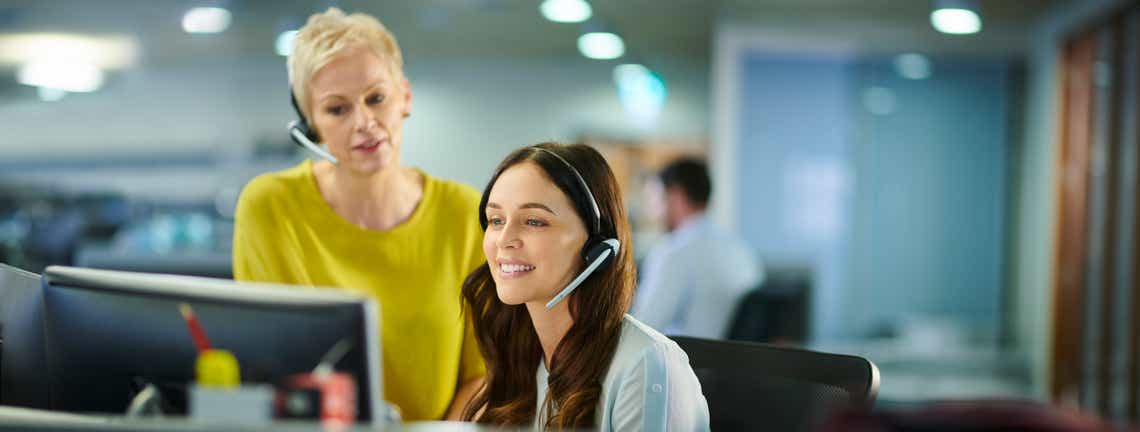 customer success associate and her manager at a computer with headsets on - practicing capabilities developed following a customer success competency framework