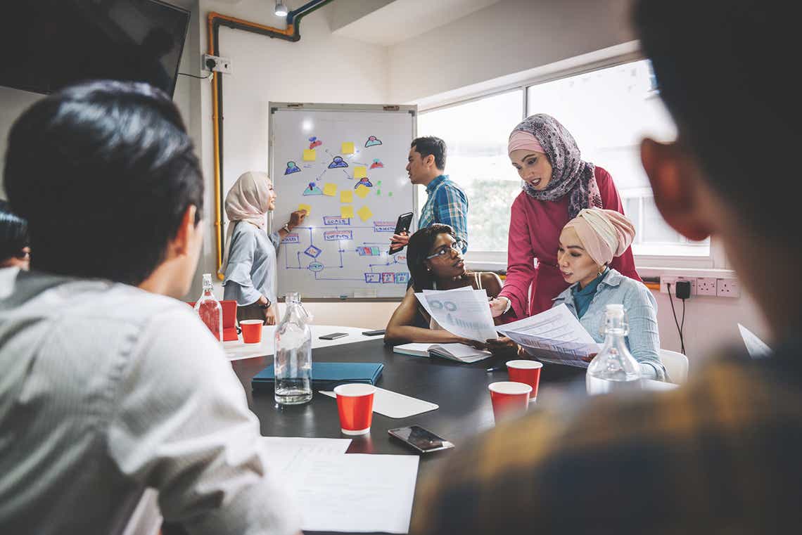 a diverse group of sellers in a corporate meeting room participating in a training program that encourages collaboration and development because of an intentional focus on the part of the program designers to consider diversity and inclusion.