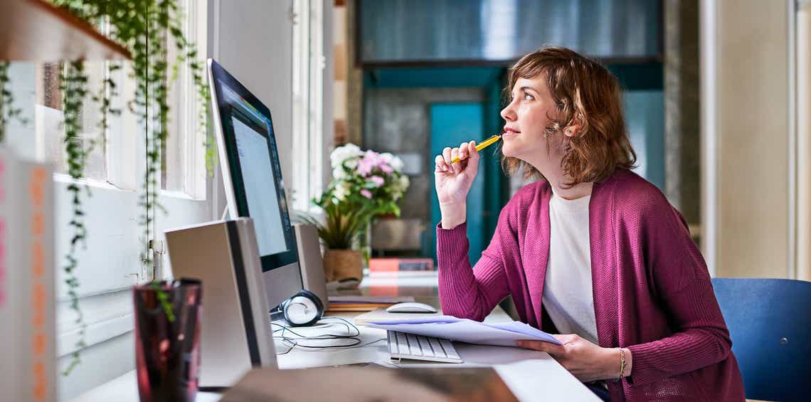a female sales manager sitting at a desk looking out the window on a sunny day, thinking about which skills to use to improve her team's performance.